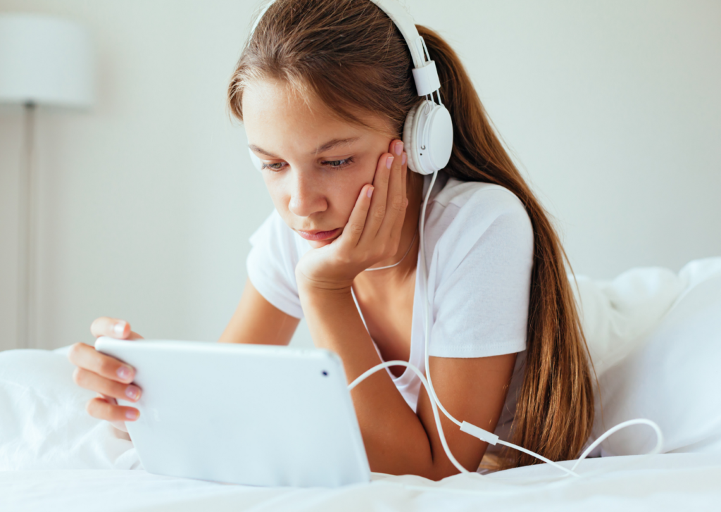 Menina na puberdade deitada em seu quarto enquanto ouve musica e usa o tablet